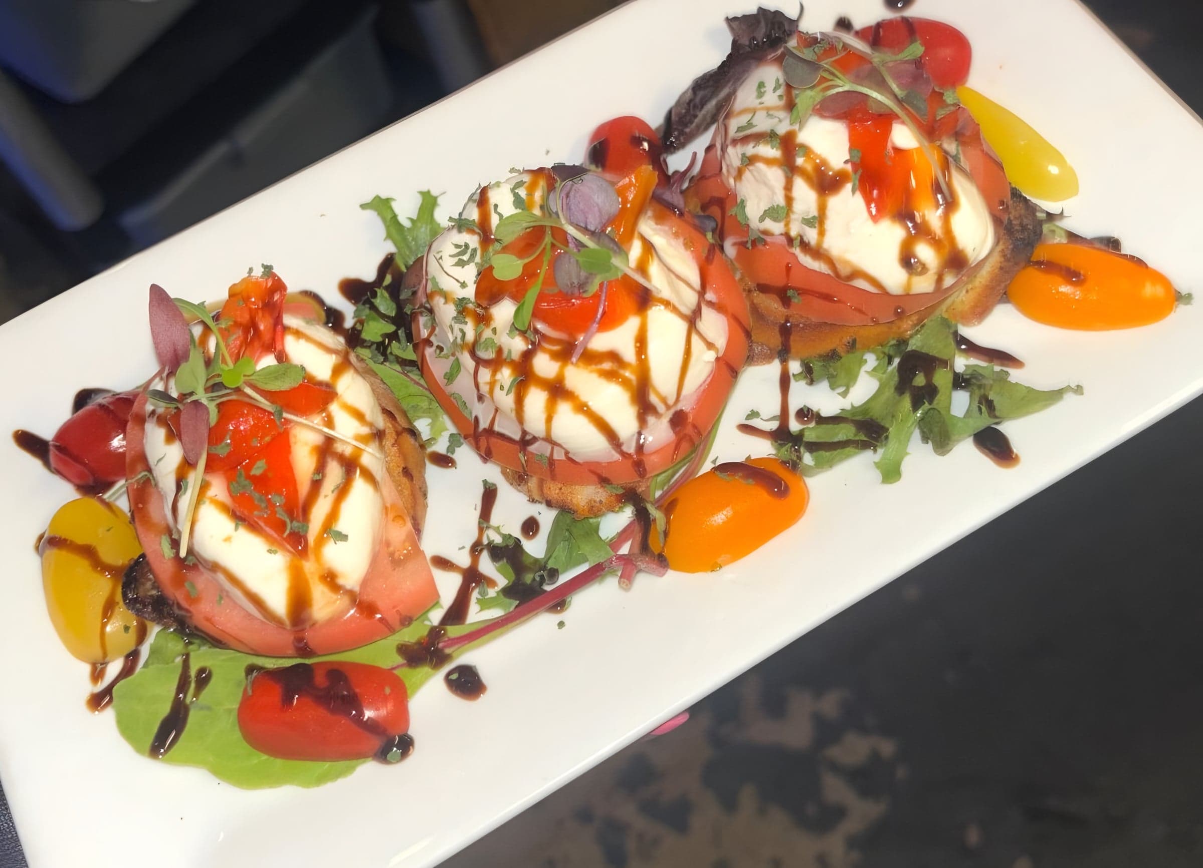 Burrata bruschetta topped with tomato, microgreens and balsamic glaze, served with heirloom cherry tomatoes and greens.