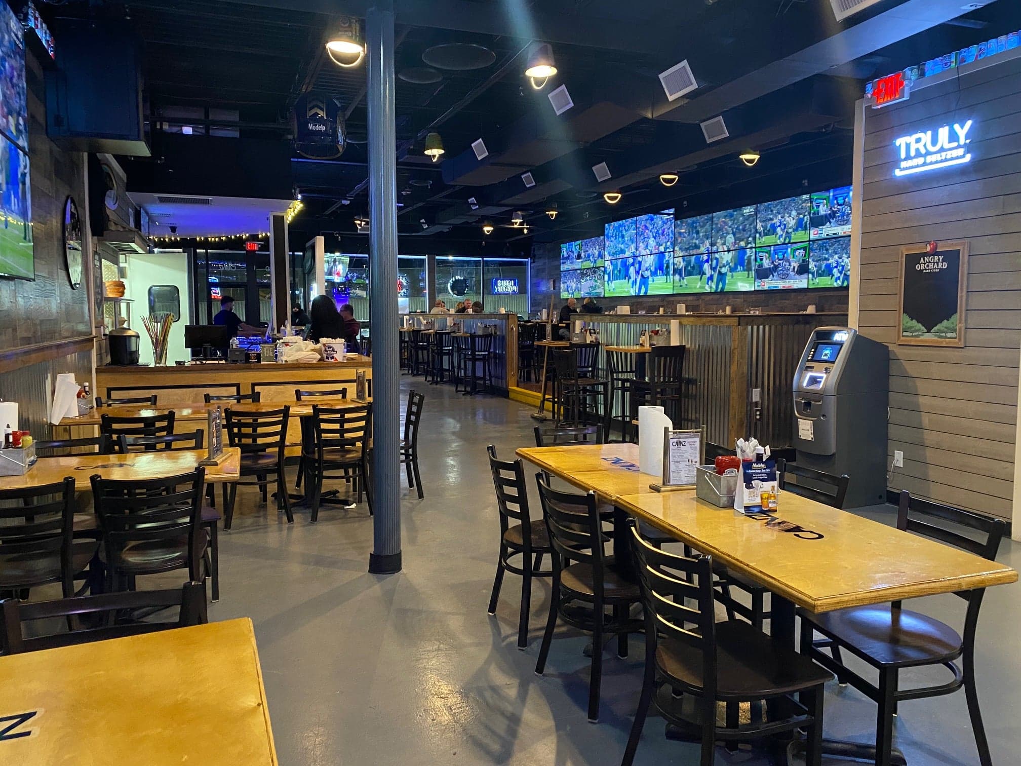 Canz Bohemia dining room with wooden tables, a high-top bar area and a wall of TVs showing football.