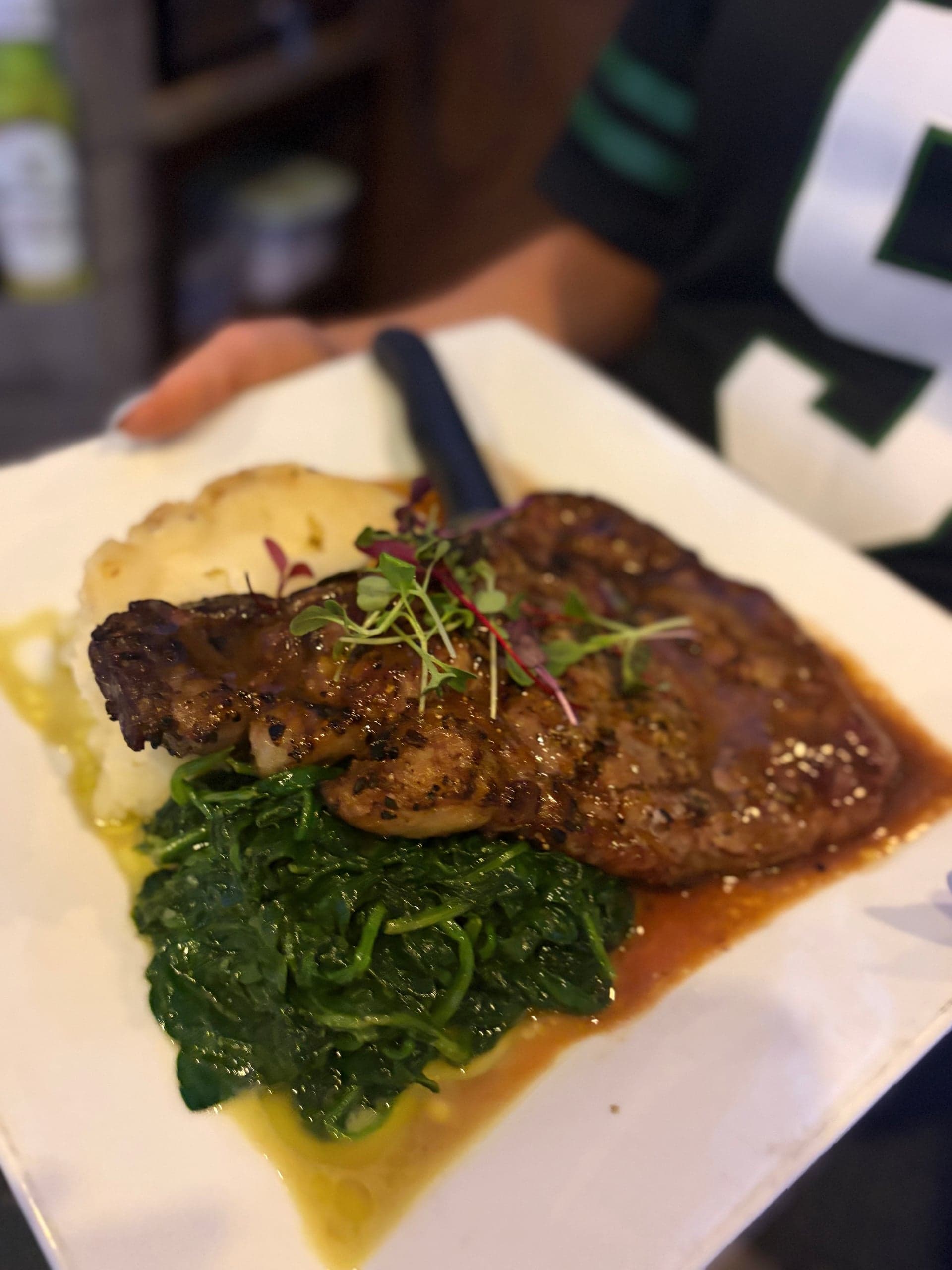 Grilled steak with pan sauce, microgreens, mashed potatoes and sautéed spinach.