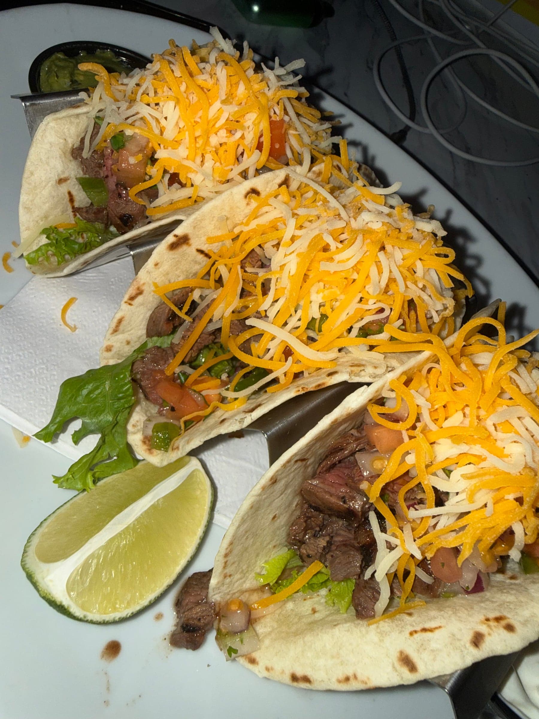Three steak tacoz on grilled flour tortillaz with pico de gallo, lettuce and shredded cheddar jack, with lime and guacamole